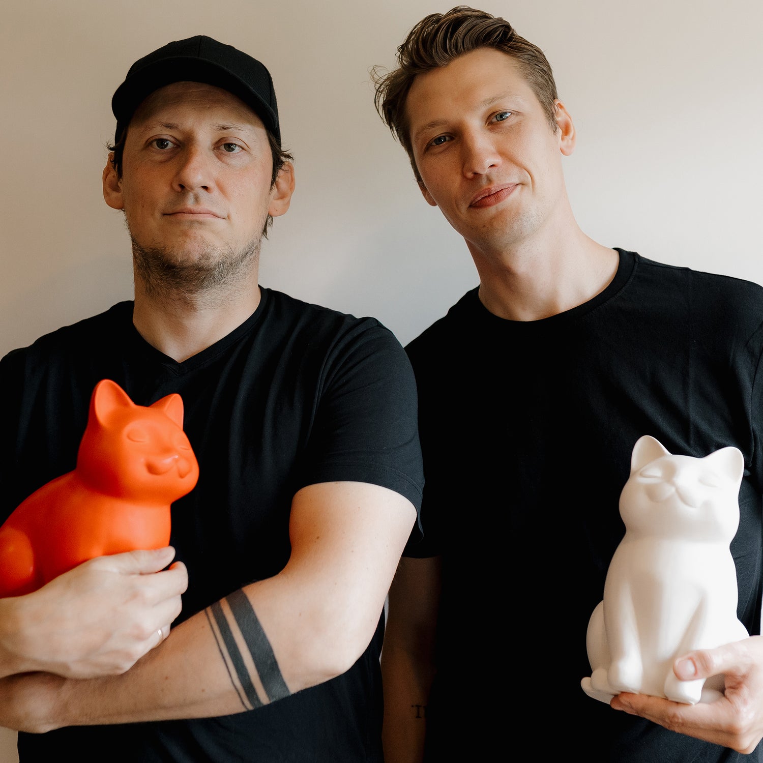 Image of two guys, owners of Paws Peace, holding personalized cat urns for ashes. Includes ceramic cat urns, wooden cat urns, black cat urn, white cat urn, sleeping cat statue urn, custom cat cremation urns, and pet urns for cats, with options like cat urn necklaces and pendants.