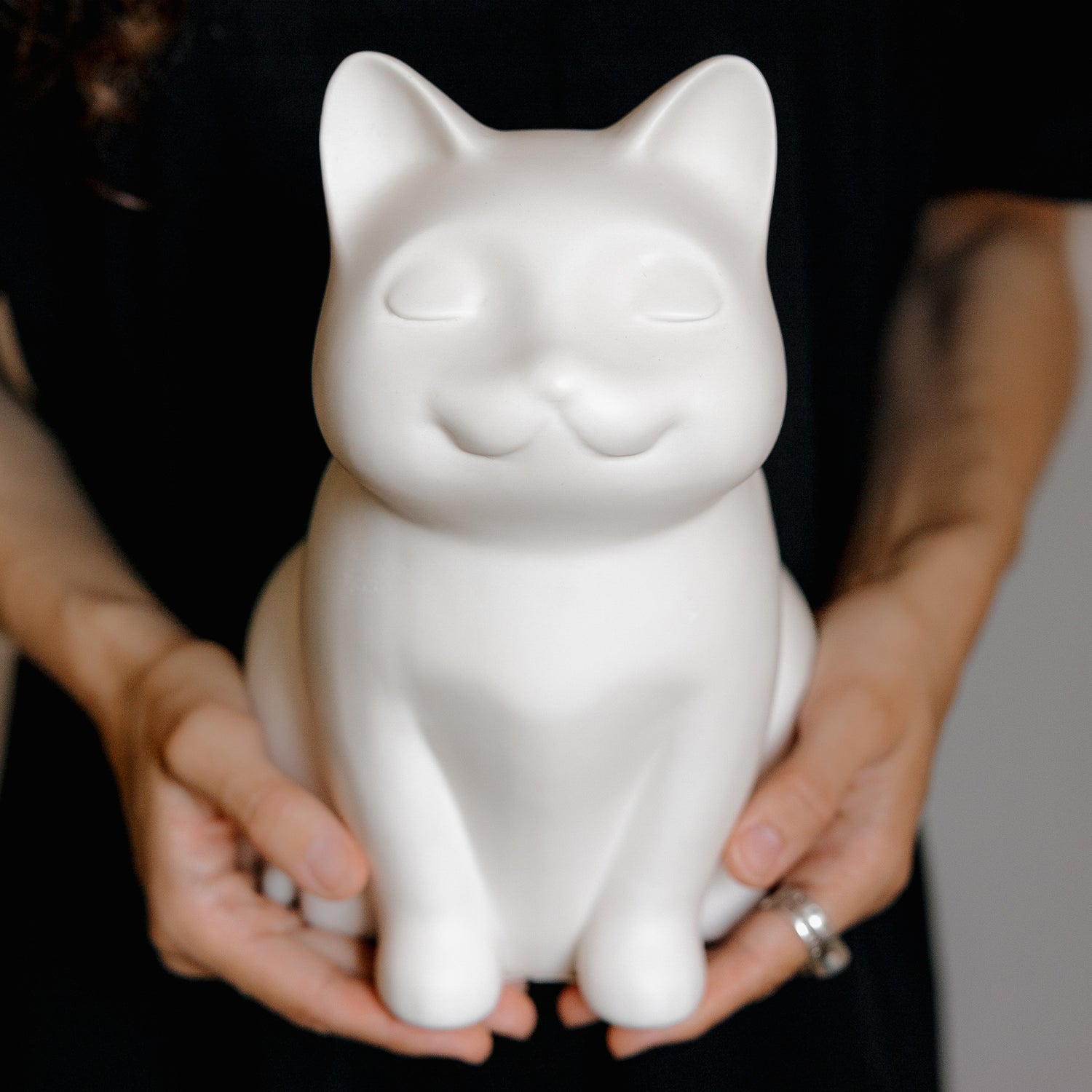 mage of women holding white pet urns for cats in their arms. Features personalized cat urns for ashes, ceramic cat urns, wooden cat urns, black cat urn, grey cat urn, custom cat cremation urns, cat-shaped urns, sleeping cat statue urn, and pet urns for cats with jewelry options like cat urn necklaces, pendants, and personalized engravable cat urns.