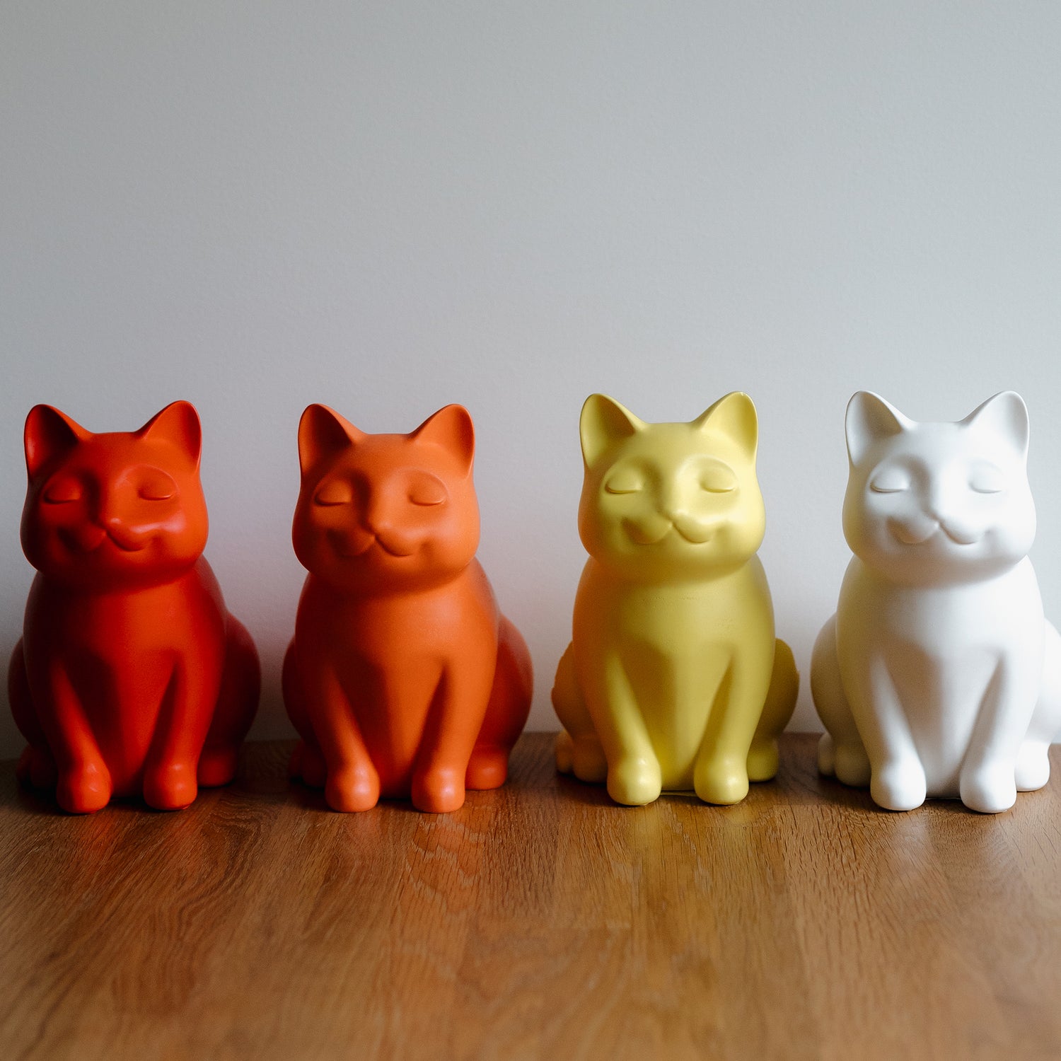 "Image of orange, red, yellow, and white ceramic cat urns standing in a line. Features personalized cat urns for ashes, acrylic cat urns, custom cat cremation urns, cat-shaped urns, sleeping cat statue urns, angel cat urns, and pet urns for cats including engravable and jewelry options like cat urn necklaces and pendants.