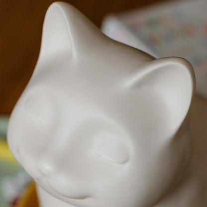 White ceramic cat urn figurine close up with eyes, ears. Features personalized cat urn for ashes, custom cat cremation urn, cat-shaped urn, sleeping cat statue urn, angel cat urn, and pet urns for cats including engravable and personalized options.