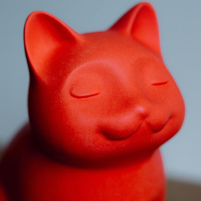Close-up of a red ceramic cat urn on a gray background. Features personalized cat urn for ashes, custom cat cremation urn, cat-shaped urn, sleeping cat statue urn, and pet urns for cats with engravable and personalized options.
